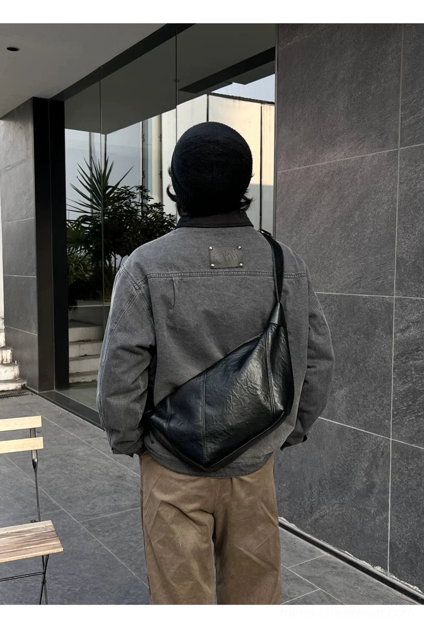Black curved PU leather crossbody sling bag worn across the back in a modern outdoor architectural setting