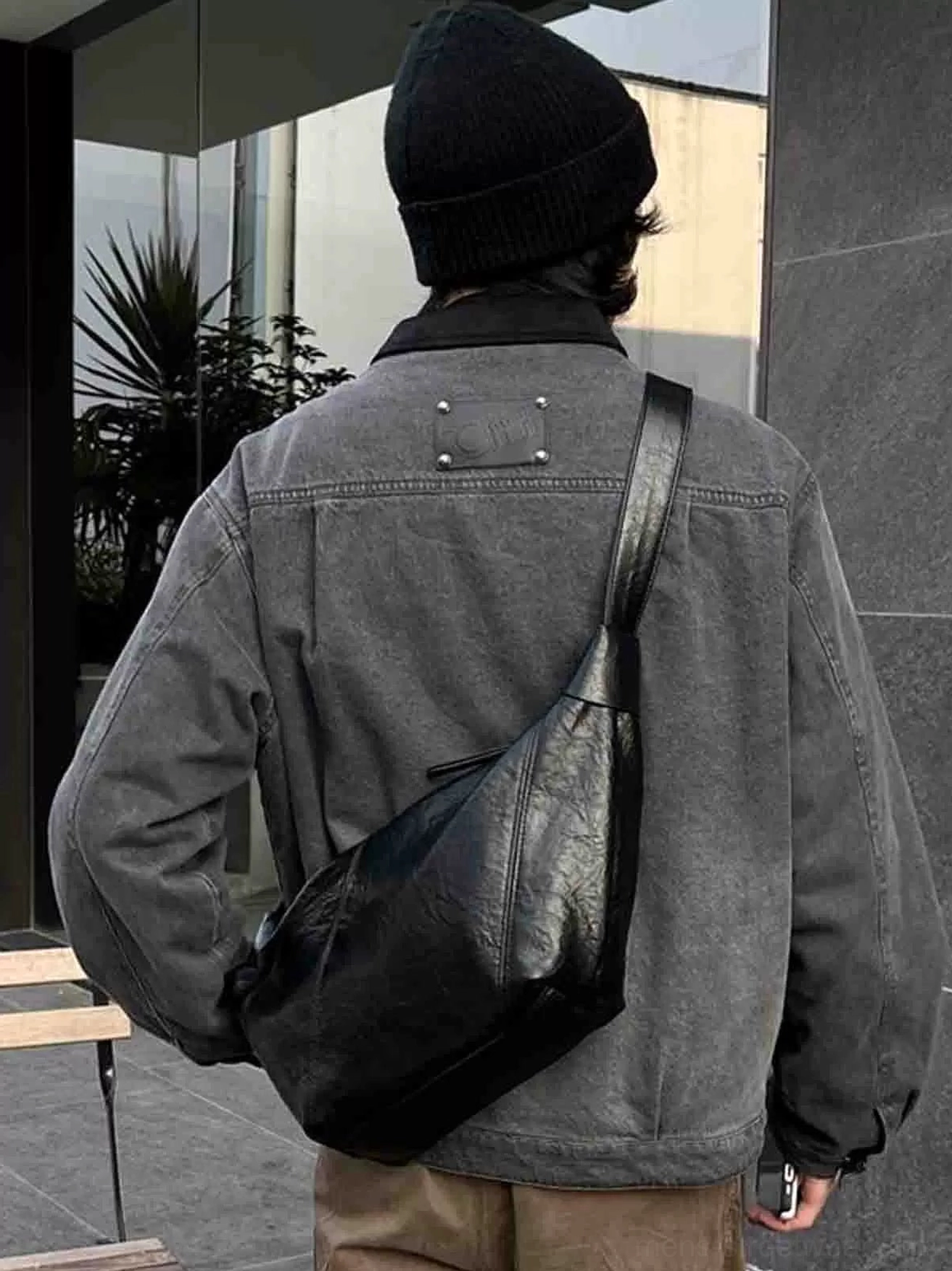 Black curved faux leather crossbody sling bag rear view with adjustable strap in modern streetwear styling