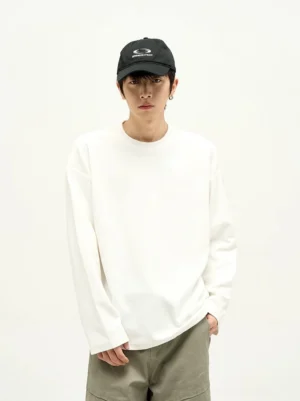 White minimalist drop shoulder cotton long sleeve crew neck t-shirt worn with khaki pants and black baseball cap