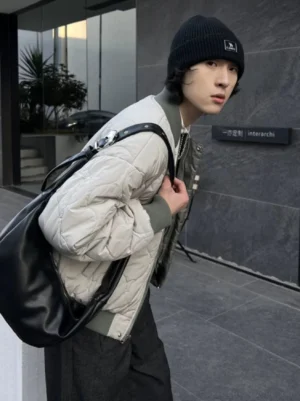 Minimalist black faux leather crescent hobo shoulder bag worn with gray bomber jacket in modern streetwear outfit