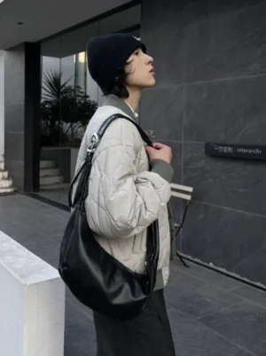 Black faux leather crescent hobo shoulder bag side profile with soft slouchy drape on male streetwear model