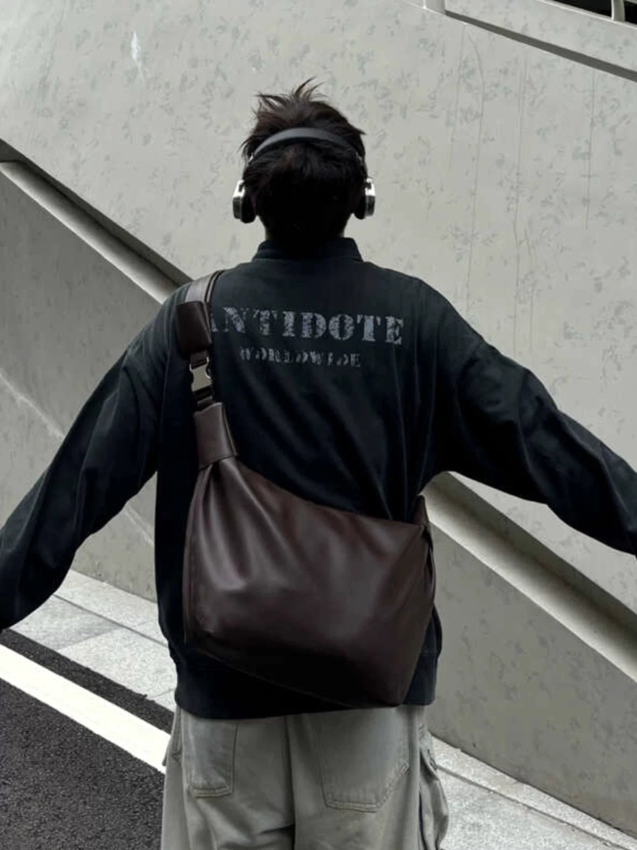 Brown minimalist crossbody shoulder sling bag with soft curved pouch silhouette and wide streetwear strap