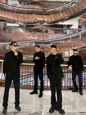 Male models wearing a minimalist black stand collar streetwear suit set with tailored jackets, ankle-cut trousers, and platform sneakers in a modern shopping mall