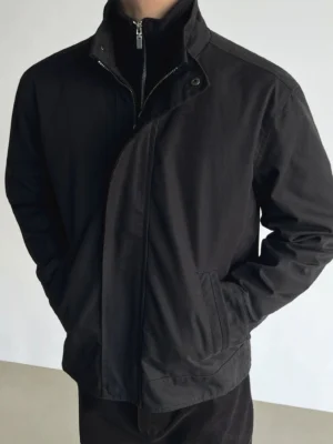 Dark charcoal black minimalist stand collar zip jacket worn by male model with black half zip knit in studio