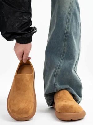 Tan suede clog mules worn with baggy jeans and black outerwear, showing the relaxed Korean streetwear slip-on silhouette and chunky rubber outsole