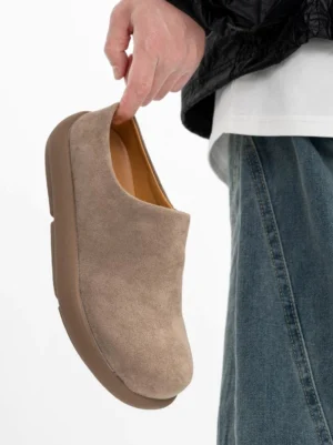 Taupe suede mule clogs shown from the side with a smooth inner lining, rounded toe, low platform sole, and minimalist streetwear design