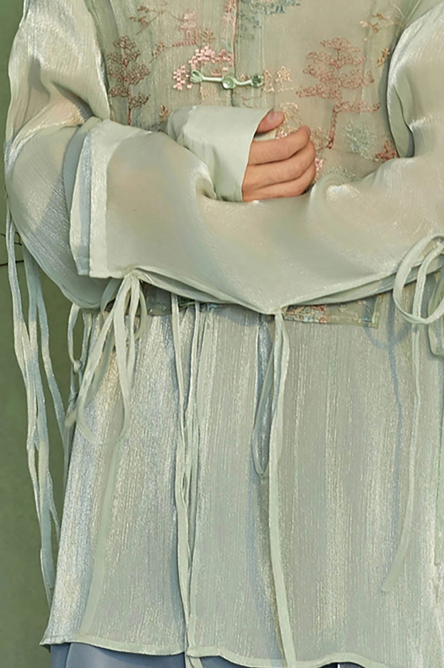 Close up of mint green Hanfu inspired jacket showing sheer sleeve fabric tassel drawstrings and embroidered vest panel