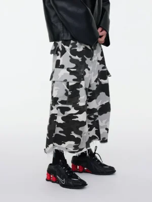 Front left three-quarter view of monochrome snow camo wide leg cropped cargo shorts styled with a black leather jacket and black sneakers with red accents