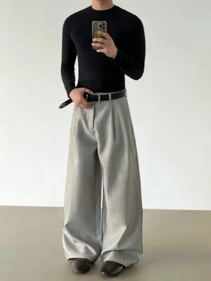 Gray pinstripe pleated wide-leg trousers in a front three-quarter mirror view styled with a black fitted knit top and brown leather shoes
