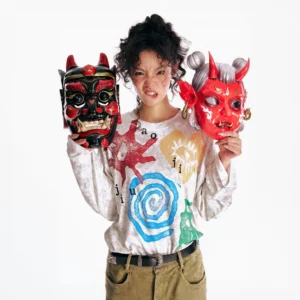 Multicolor washed tribal graphic oversized long sleeve tee on female model holding traditional folk masks in a white studio