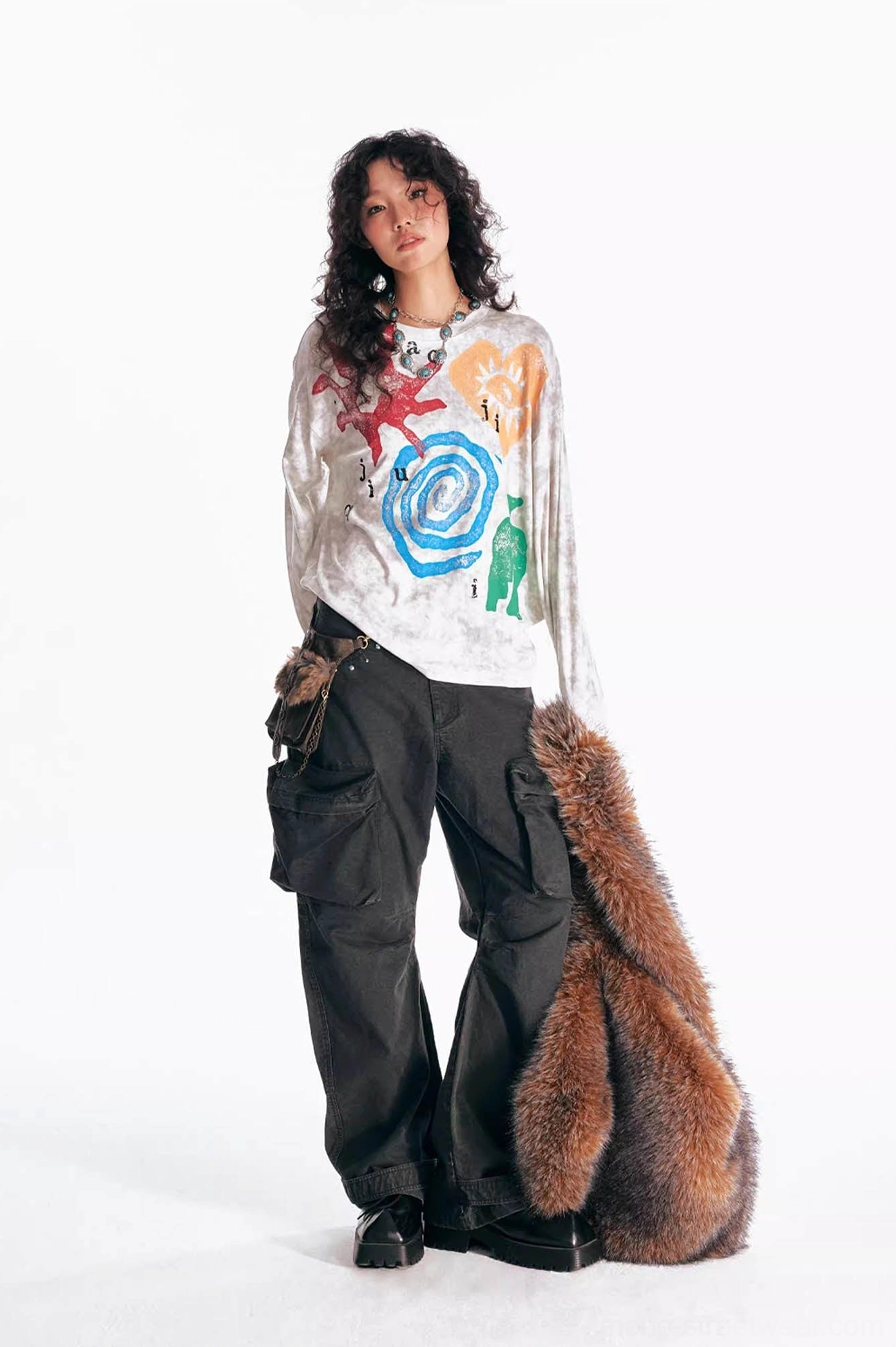 Female model wearing multicolor washed tribal graphic oversized long sleeve tee with black cargo pants and furry crossbody bag