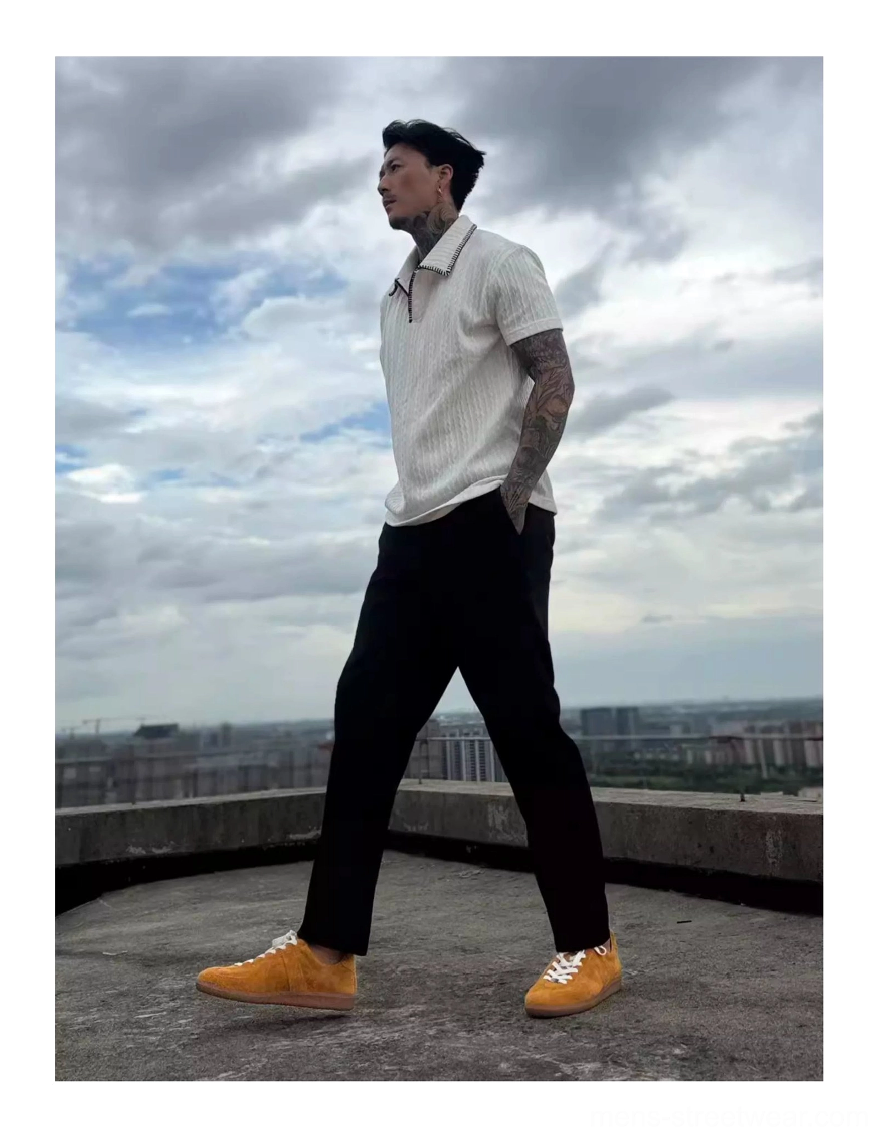 Model styling mustard suede heritage sneakers with white polo shirt and black tailored trousers on urban rooftop