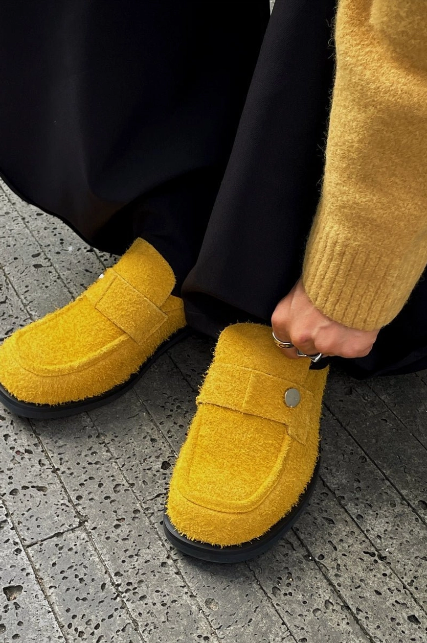 Close-up of mustard yellow suede penny loafers worn with black wide-leg pants and a mustard knit sweater on a city sidewalk