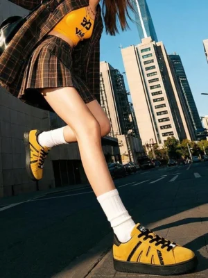Mustard yellow suede platform sneakers styled with cropped plaid streetwear clothing and white crew socks on an urban downtown street