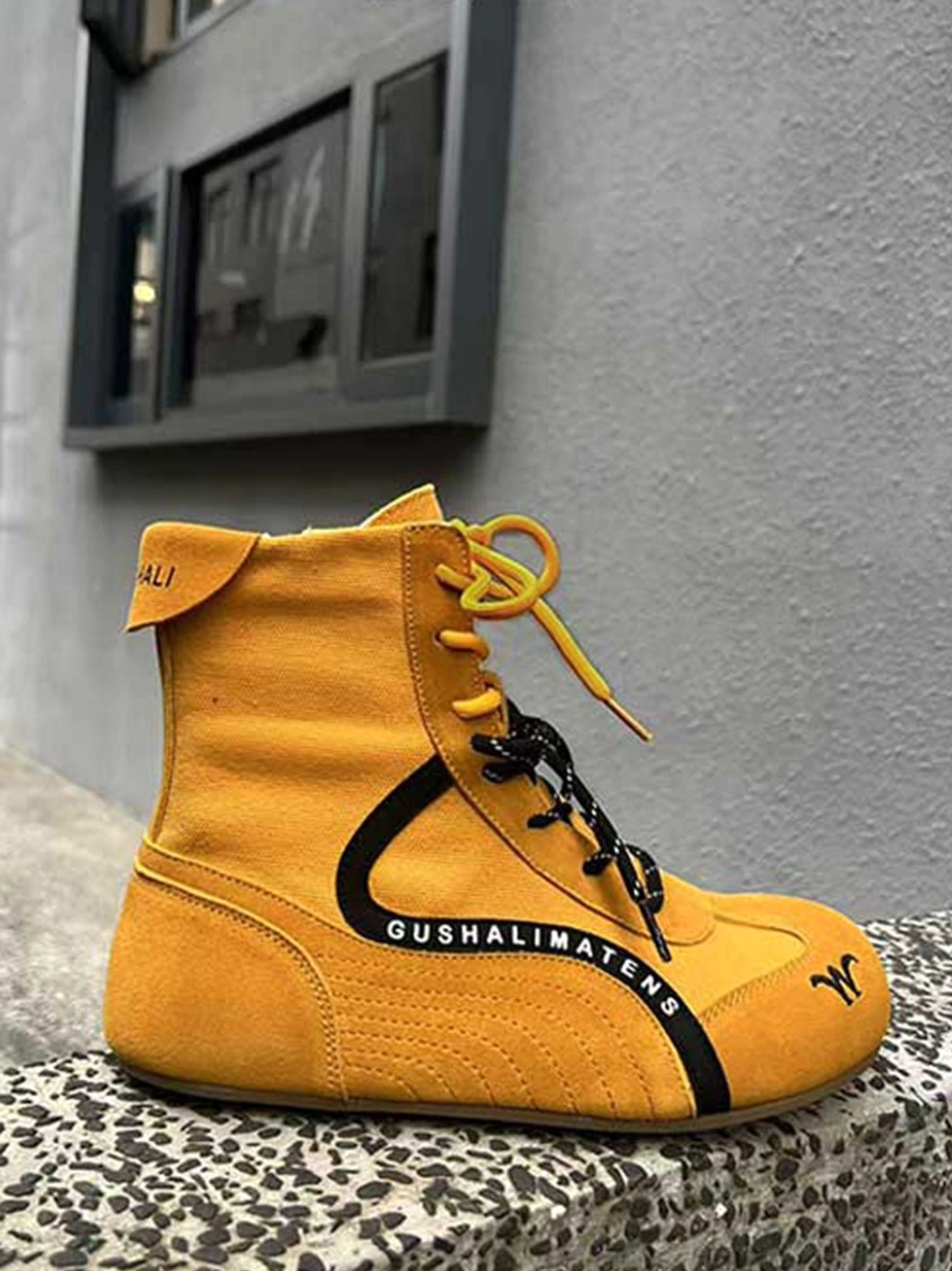 Mustard yellow high-top suede racing boots with black contrast stripe, dual colored laces, side text detail, and heel pull tab