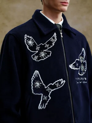 Close-up of navy bird embroidered zip-up jacket showing flying bird artwork lettering zipper and soft textured fabric