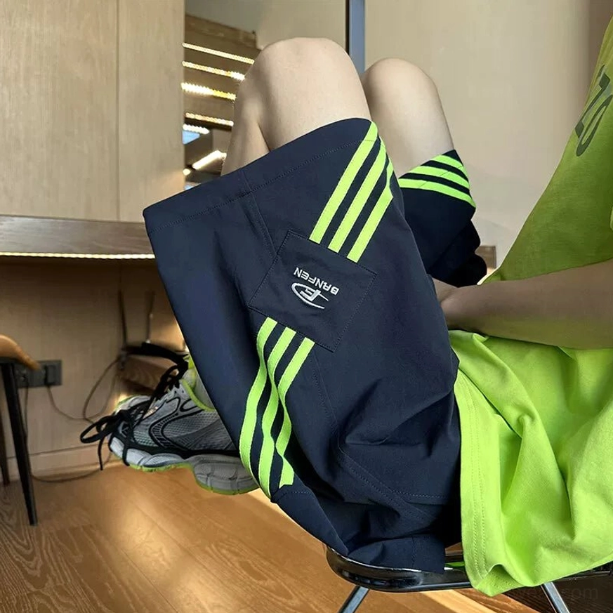 Navy blue Acubi streetwear sports shorts with neon green three-stripe side trims, oversized neon tee, and chunky athletic sneakers