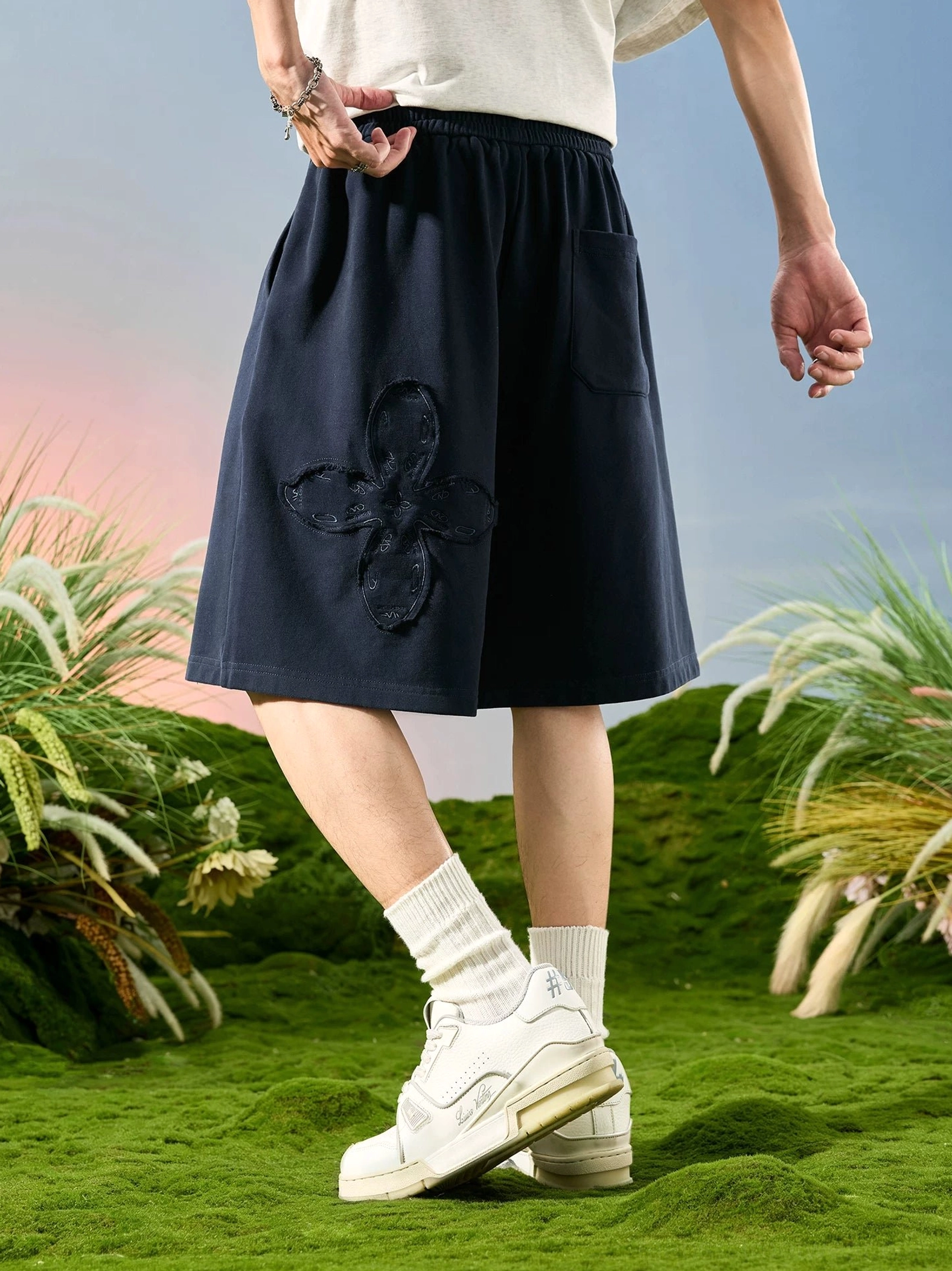 Navy blue floral appliqué relaxed sweat shorts shown in a low rear side view with wide-leg streetwear fit