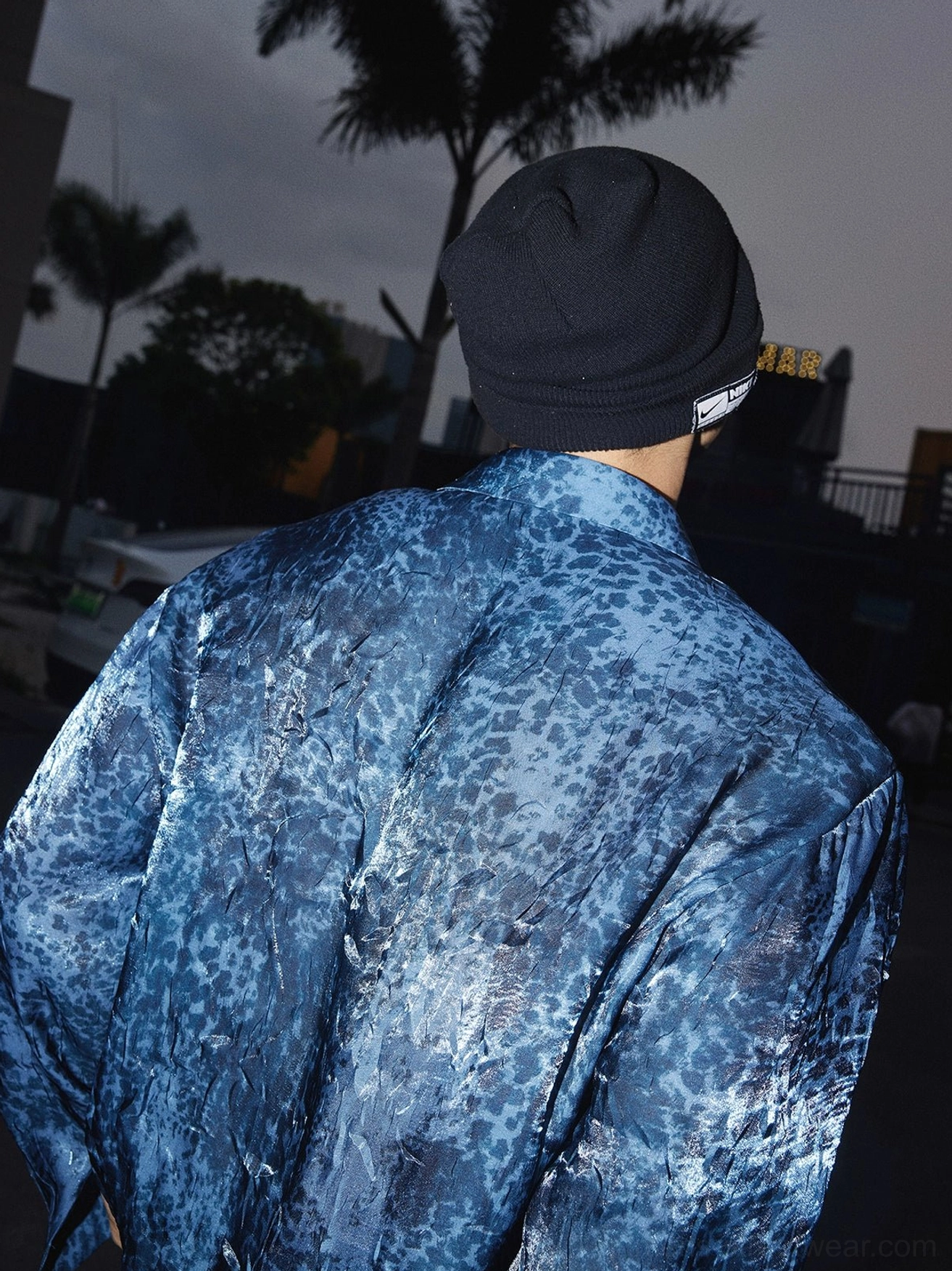 Back view of a navy blue glossy leopard print long-sleeve button-up streetwear shirt showing the relaxed oversized silhouette in an urban nighttime setting
