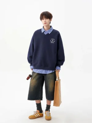 Navy blue oversized V-neck sweatshirt styled with a striped shirt, wide-leg denim shorts, casual sneakers, and tote bag