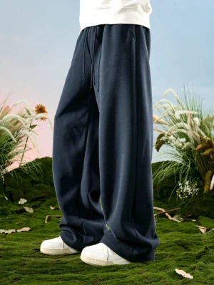 Navy blue relaxed wide-leg sweatpants shown from the side with an elastic drawstring waist and casual sneakers