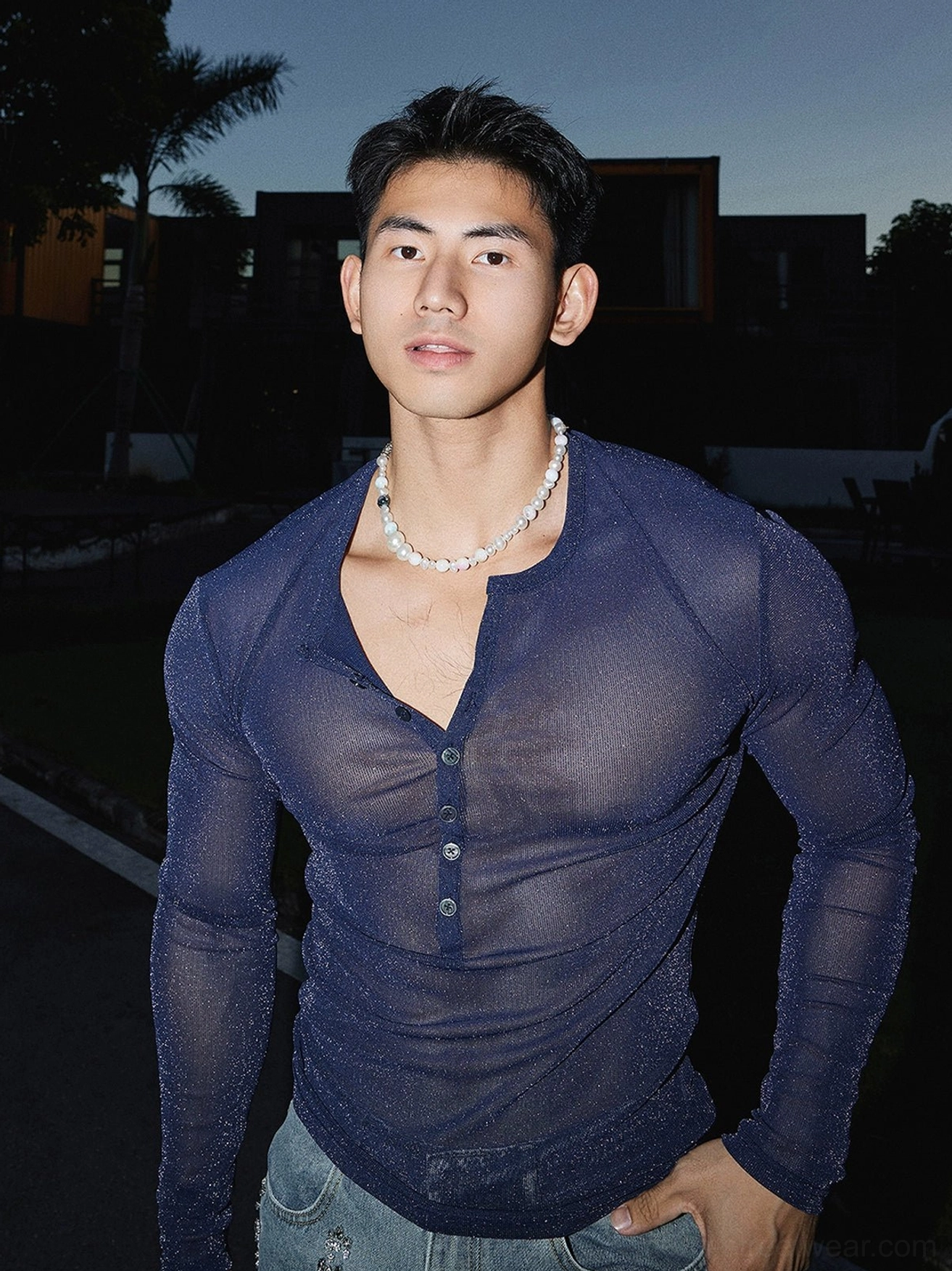 Front close-up of a male model wearing a navy blue sheer sparkly Henley top with pearl necklace and blue jeans