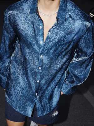 Front view of a navy blue shiny leopard print oversized button-up streetwear shirt with long sleeves, white buttons, relaxed fit, and open collar styled for nighttime urban fashion