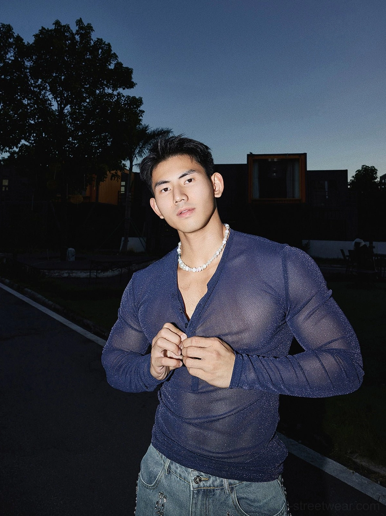 Close-up of a male model adjusting the button placket on a navy blue slim fit sheer sparkly Henley streetwear top