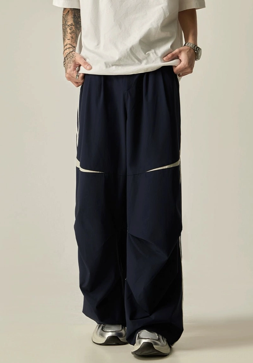 Navy blue ultra-wide track pants featuring a pleated front waist, smooth matte fabric, and relaxed streetwear proportions
