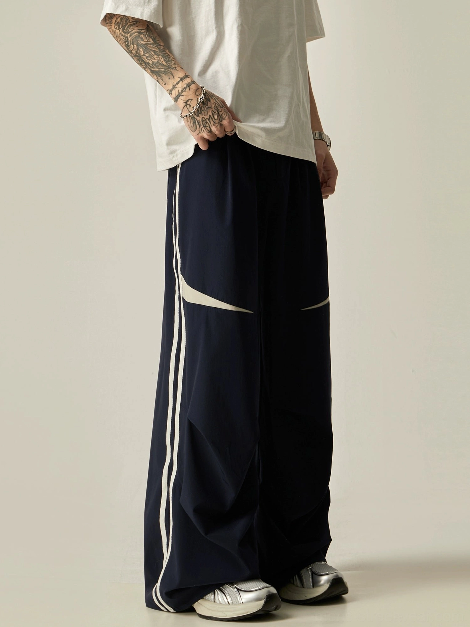 Side view of navy blue dual-stripe wide-leg track pants with white curved panels and fluid drapey streetwear fabric