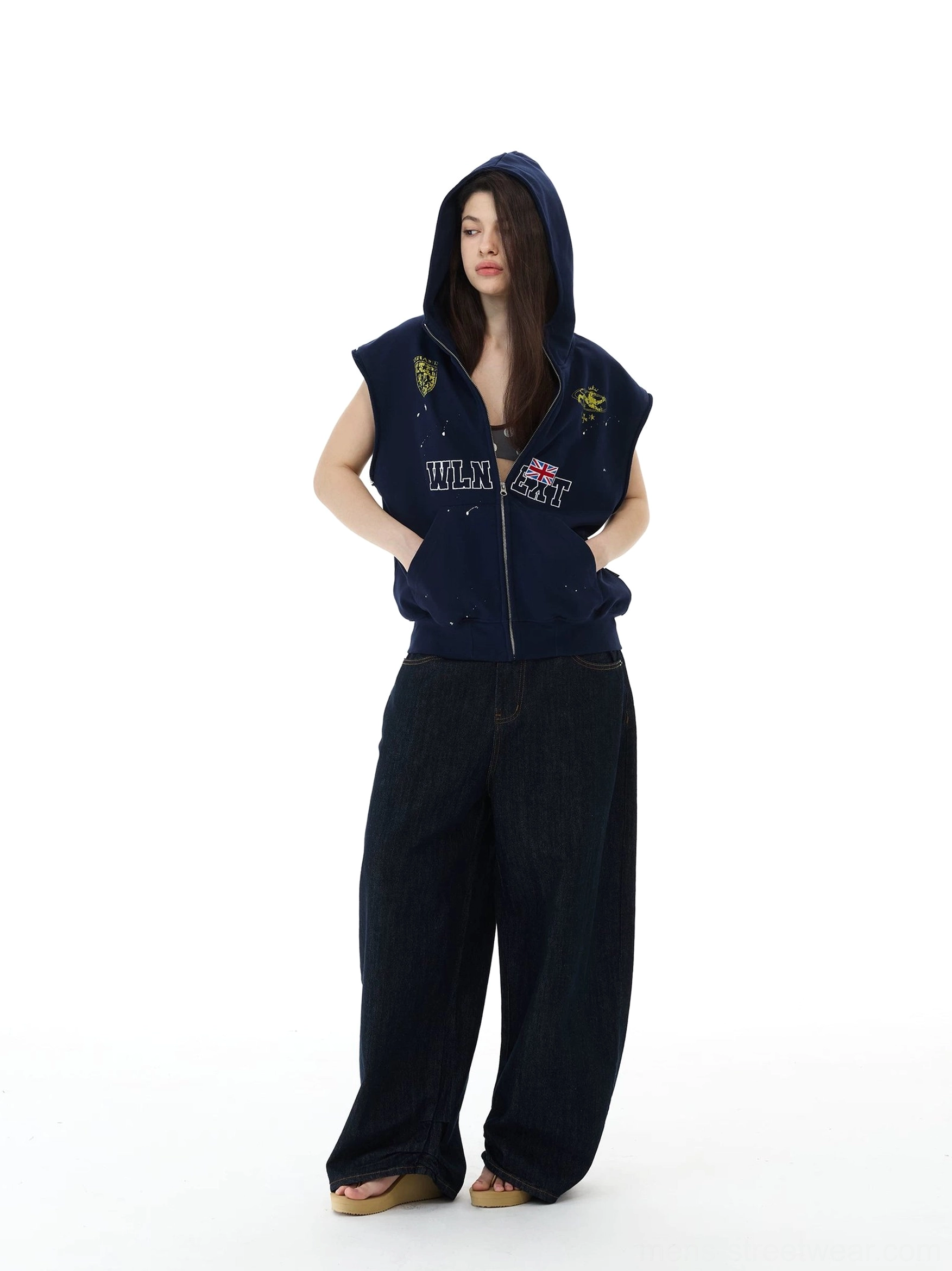 Front full body view of navy splatter graphic sleeveless zip hoodie vest styled with wide leg black jeans