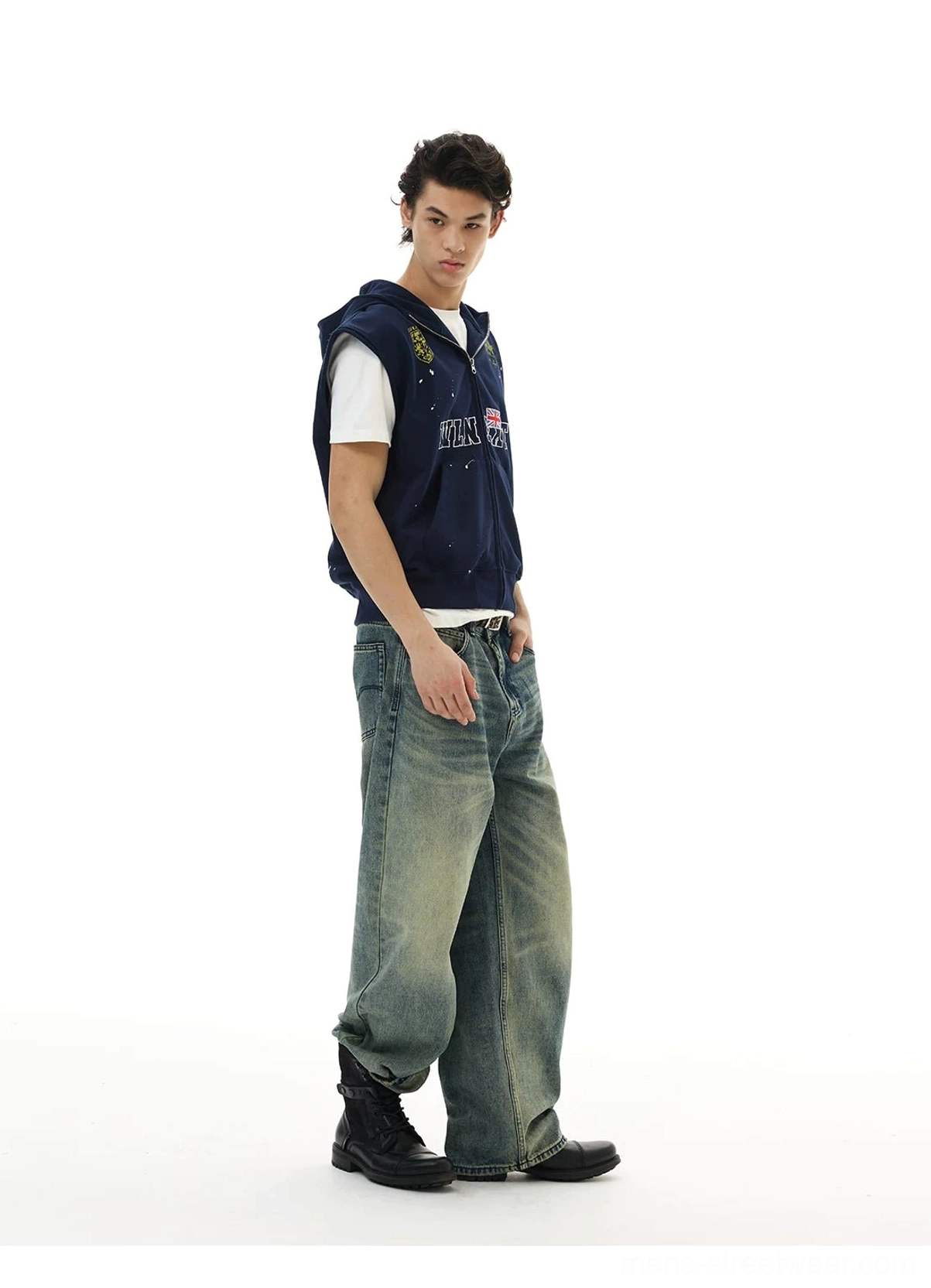 Side view of navy collegiate crest sleeveless zip hoodie vest layered over white t-shirt with washed jeans and boots
