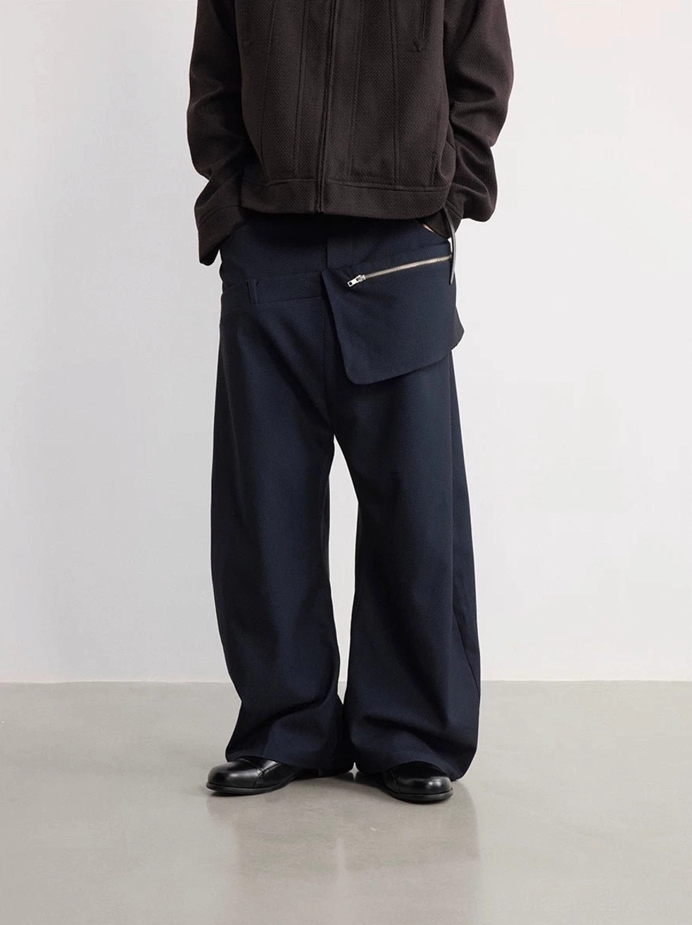 Rear view of navy detachable zipper pouch wide-leg trousers styled with a dark brown zip-up jacket and leather dress shoes