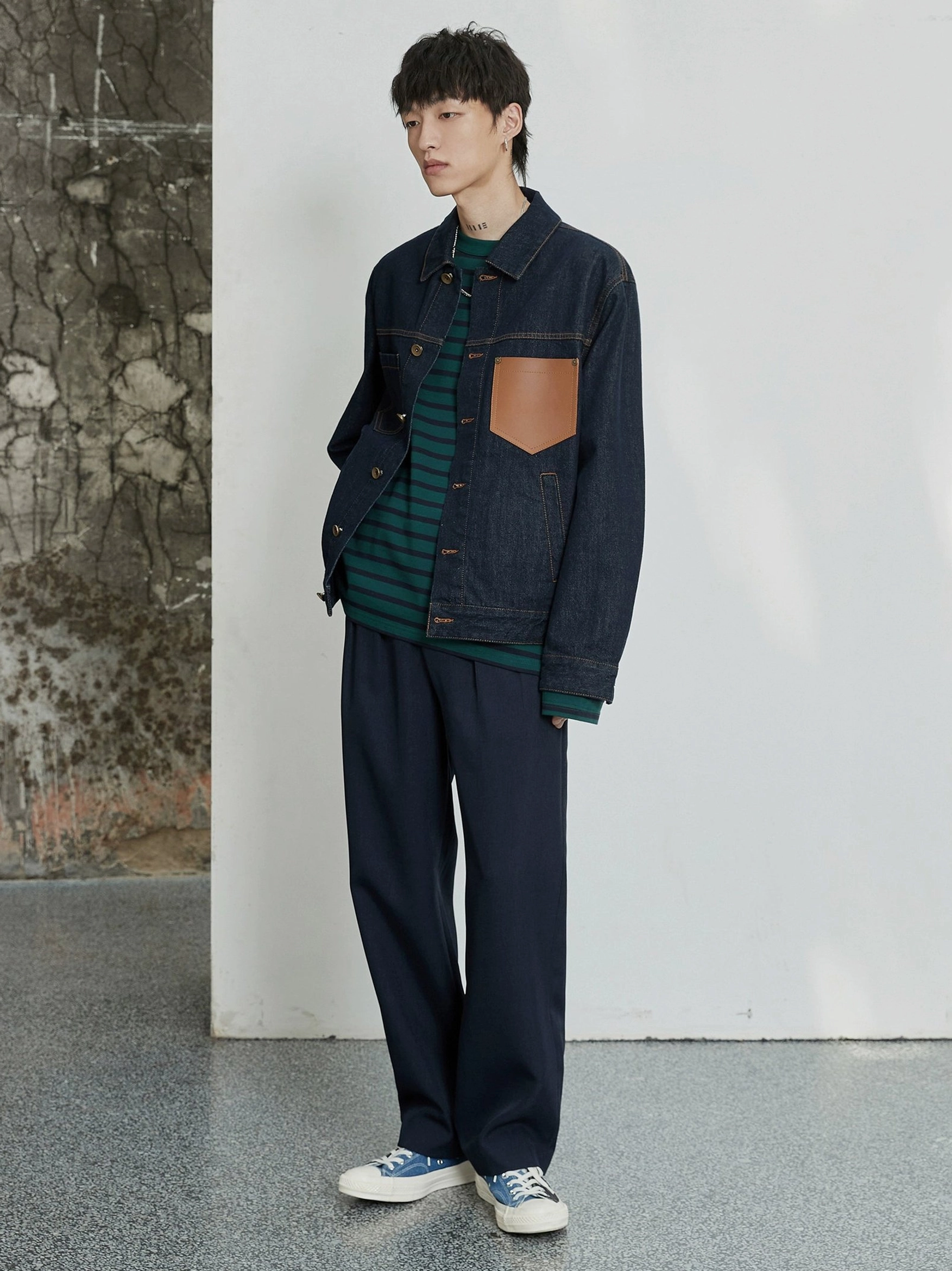 Navy double-pleated dress pants styled with a denim jacket and canvas sneakers in a casual streetwear outfit