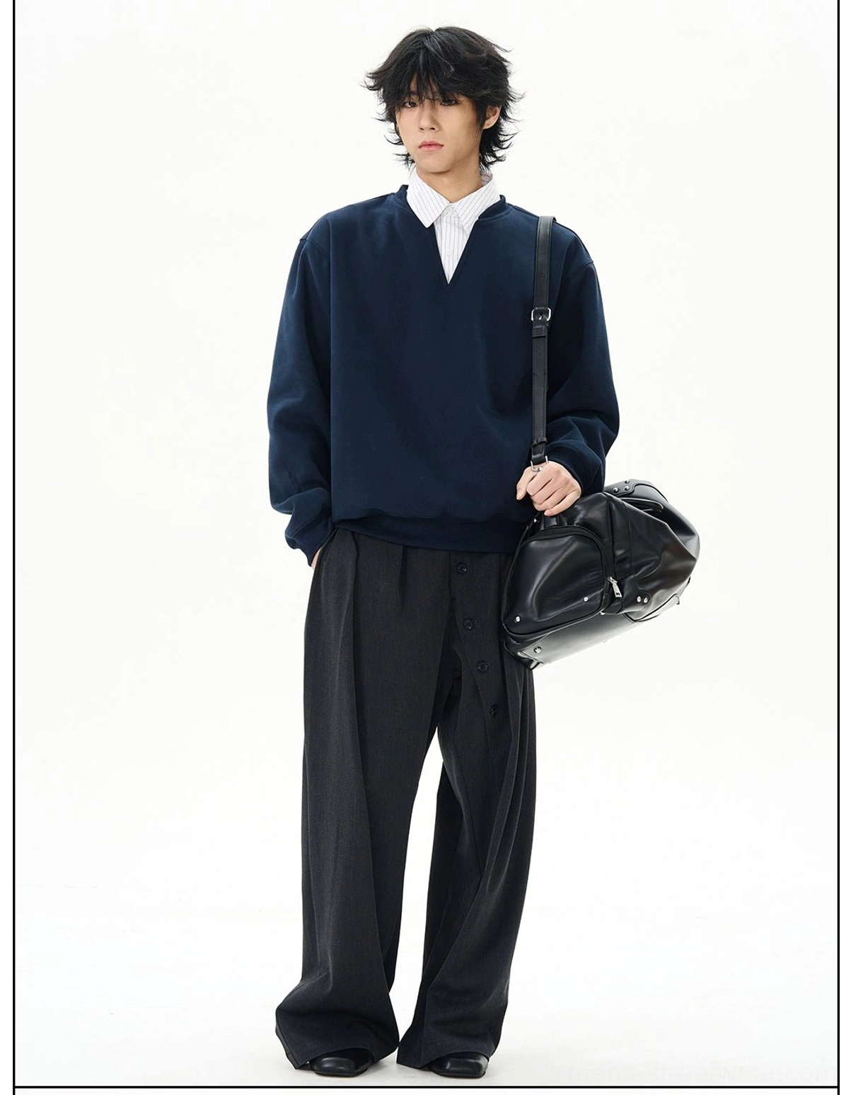 Three-quarter view of navy oversized streetwear sweatshirt styled with wide-leg black trousers and a black leather duffel bag