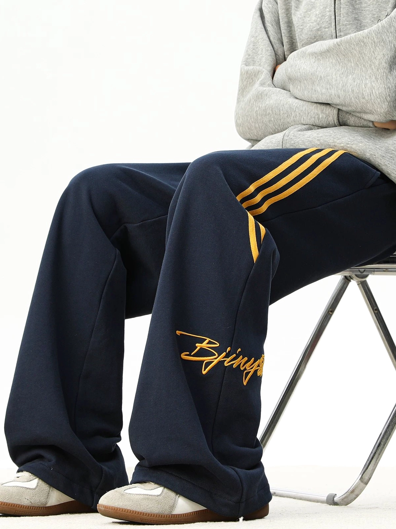 Navy oversized striped sweatpants with golden yellow side stripes and matching embroidery, styled with a hoodie and sneakers for a relaxed Seoul streetwear outfit