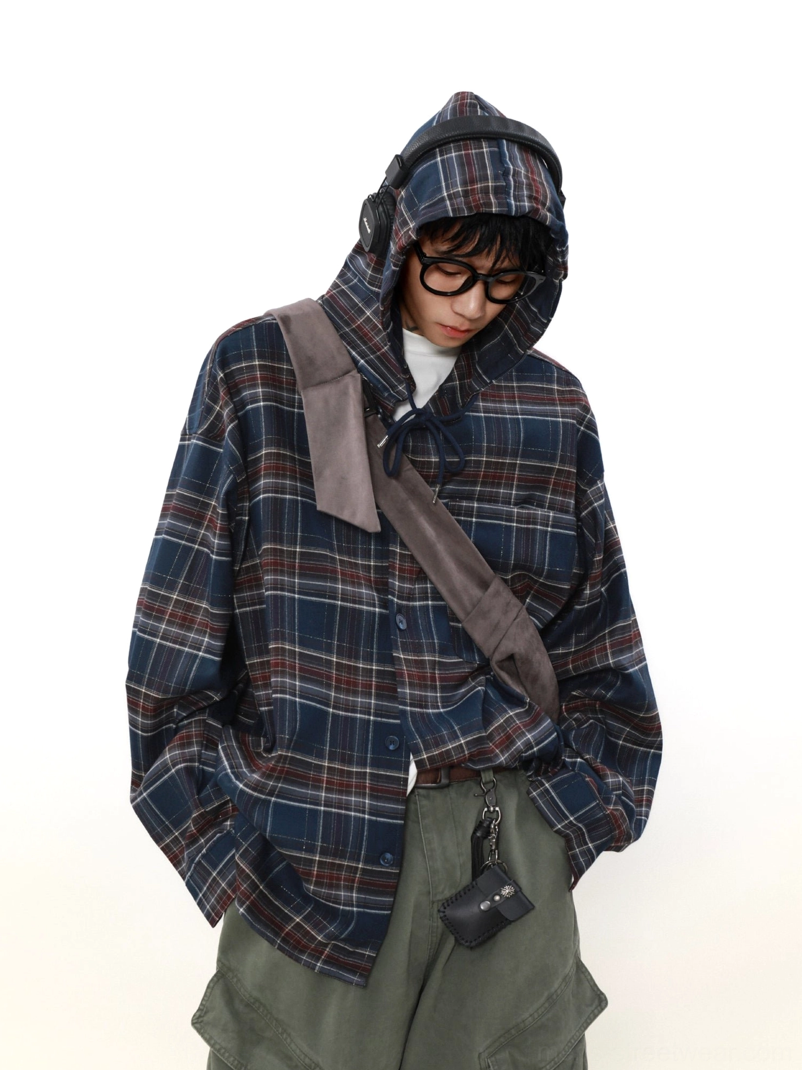 Male model wearing a navy plaid hooded streetwear shirt with the drawstring hood up and crossbody accessories in a relaxed three-quarter view