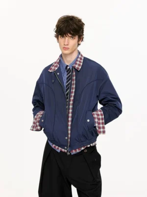 Navy blue plaid-lined cropped Harrington jacket worn by male model with black wide-leg trousers layered check shirt and striped tie
