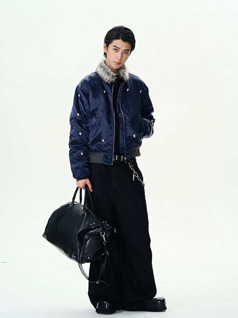 Full body side view of a navy satin bomber jacket styled with black wide-leg trousers leather tote and chain belt