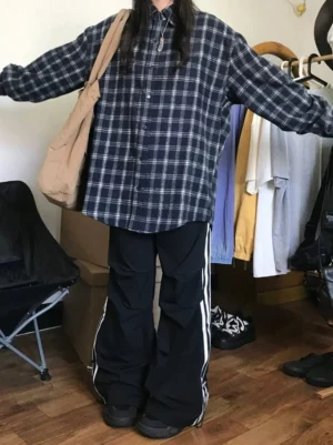 Full front view of navy and white plaid oversized flannel shirt styled with wide-leg side stripe track pants