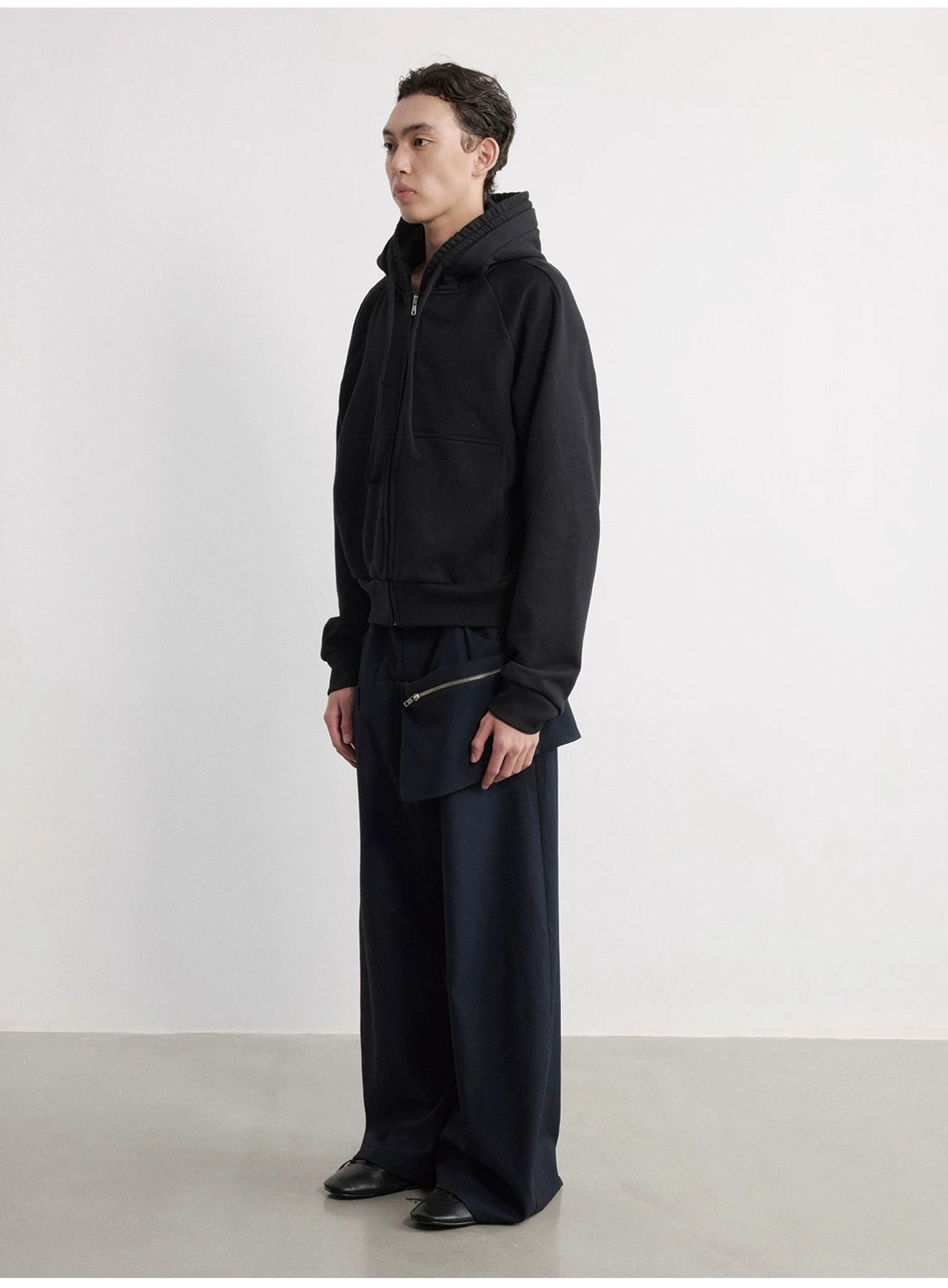 Male model holding the removable pouch from navy zipper pocket wide-leg trousers in Seoul streetwear styling