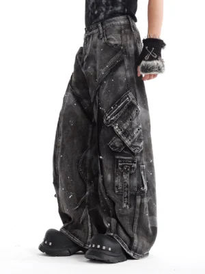 Side view of gray baggy cargo denim jeans showing layered tactical pockets, seam panels, straps, and faded splatter wash