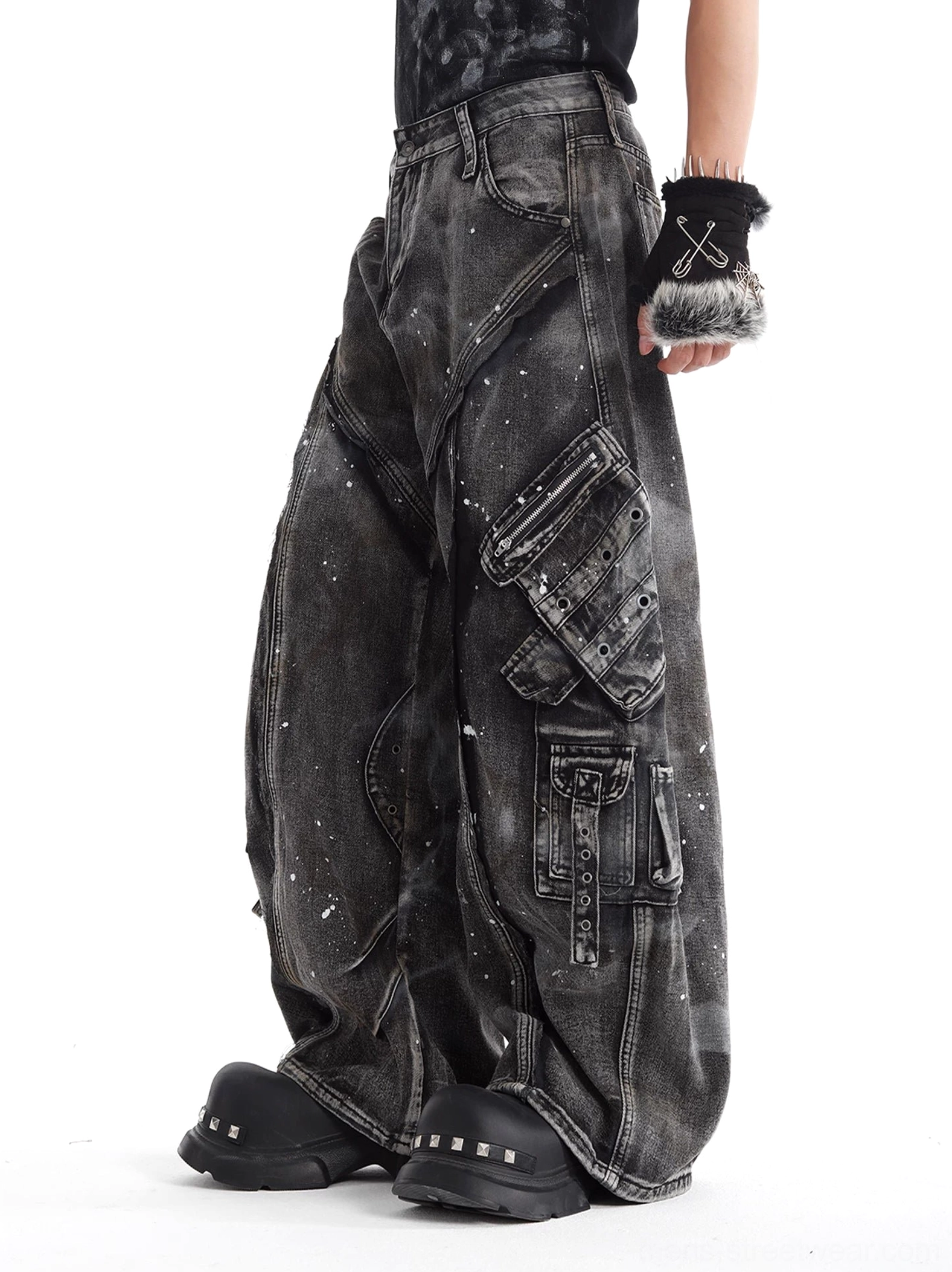 Side view of gray baggy cargo denim jeans showing layered tactical pockets, seam panels, straps, and faded splatter wash