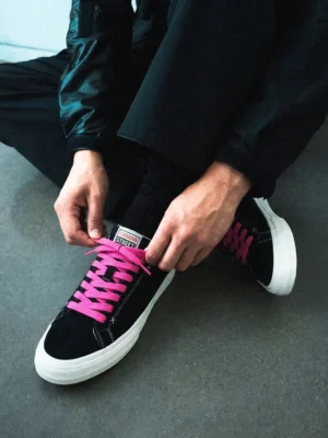 Close-up of black suede platform sneakers with neon laces being tied with black trousers for modern streetwear fashion