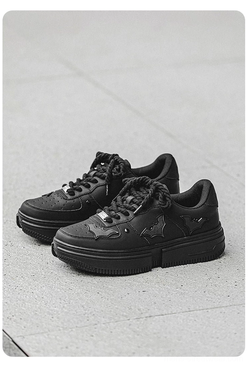 Flat lay of two pairs of black bat crest platform sneakers showing split chunky soles and side bat appliqué details