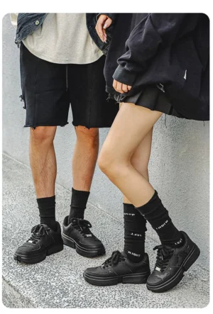 Couple wearing matching black bat crest platform sneakers styled with casual monochrome streetwear and crew socks