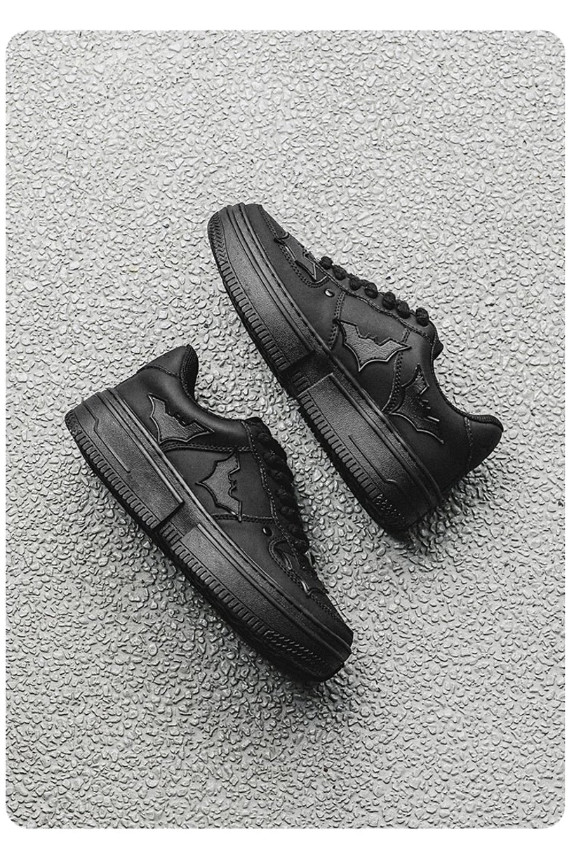 Overhead view of black Nightwing bat crest platform sneakers on textured concrete displaying the outsole and bat emblem upper