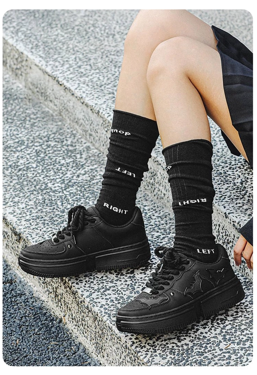 Black bat crest platform sneakers worn with a short skirt and graphic crew socks on concrete stairs