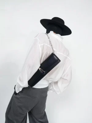 Back view of obsidian black chain shoulder clutch bag styled with white shirt and grey trousers for Seoul streetwear