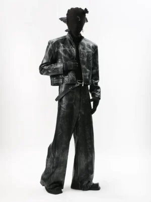 Left three quarter view of a black distressed faux leather moto jacket and matching wide leg pants set with cropped stand collar, acid washed texture, contrast stitching, leather belt, tactical gloves, and avant garde streetwear styling